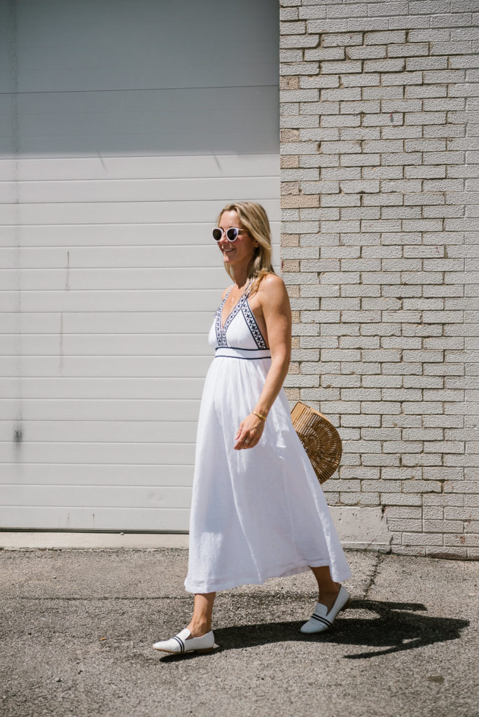 woman wearing one of the white summer dresses, white shoes, and holding a handbag woman walking and wearing white dress, white flats, and a bag