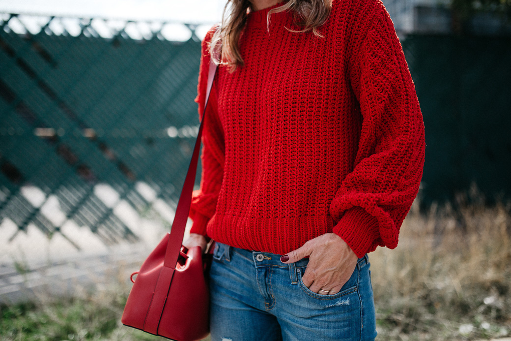 a red sweater and a red purse that you need for fall, along with blue jeans, 5 Sweaters Needed For Fall