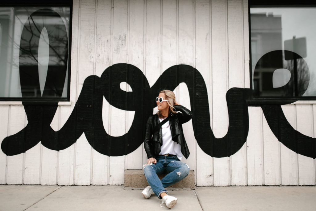 Love mural background dressed in denim, white logo tee, sneakers and leather jacket