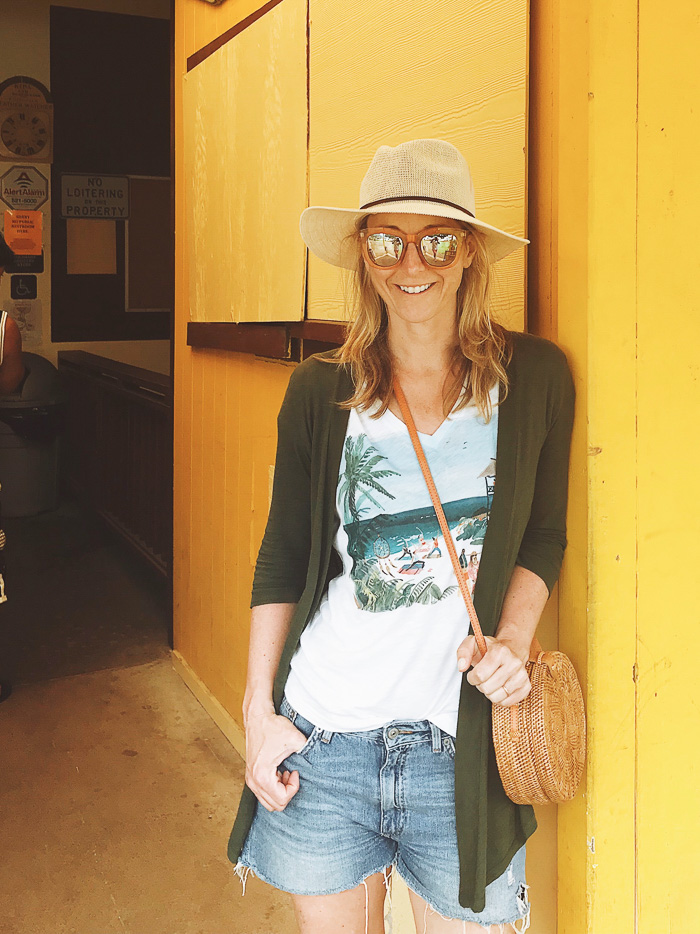 woman wearing Denim Shorts, White Graphic Tee, Panama Hat, Straw Purse, Moss Green Cardigan woman wearing Denim Shorts, White Graphic Tee, Panama Hat, Straw Purse, Moss Green Cardigan