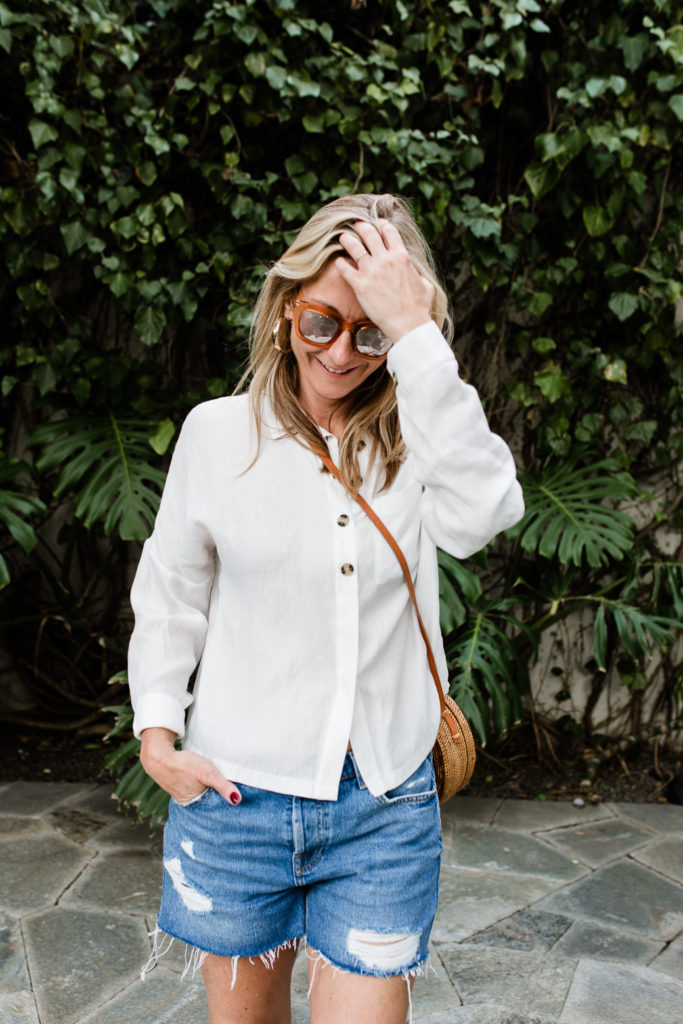 woman smiling and wearing denim shorts and White Essentials for Spring woman smiling and wearing denim shorts and White Essentials for Spring